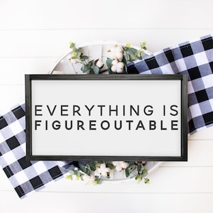 May include: A black framed sign with white background and the text "EVERYTHING IS FIGUREOUTABLE" in black lettering. The sign is surrounded by white cotton balls and green leaves.