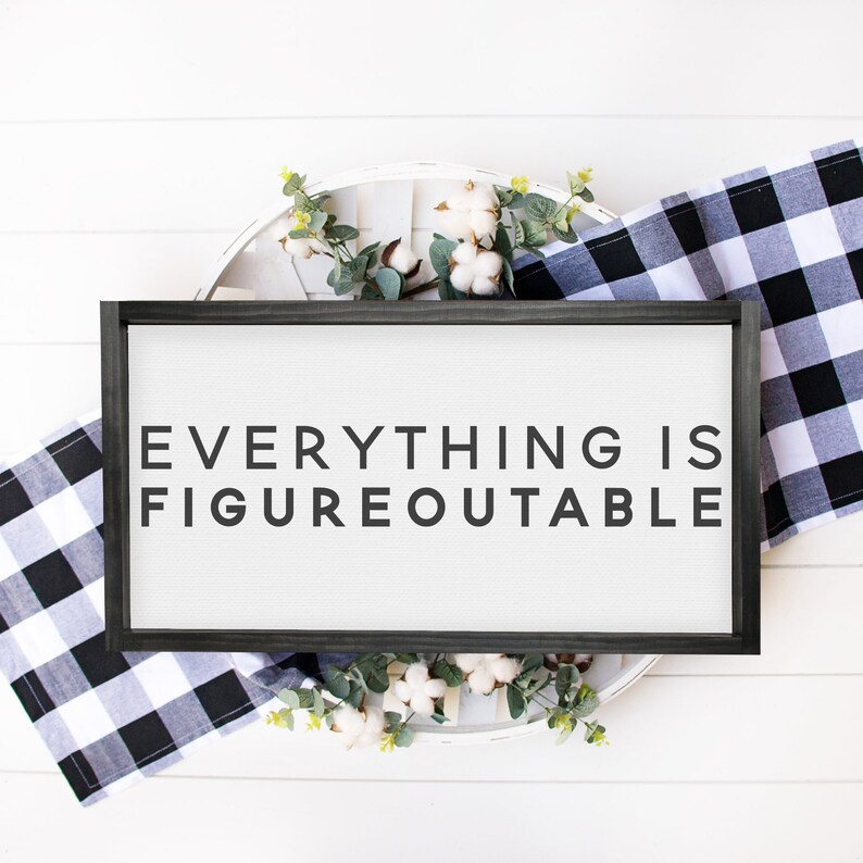 May include: A black framed sign with white background and the text "EVERYTHING IS FIGUREOUTABLE" in black lettering. The sign is surrounded by white cotton balls and green leaves.