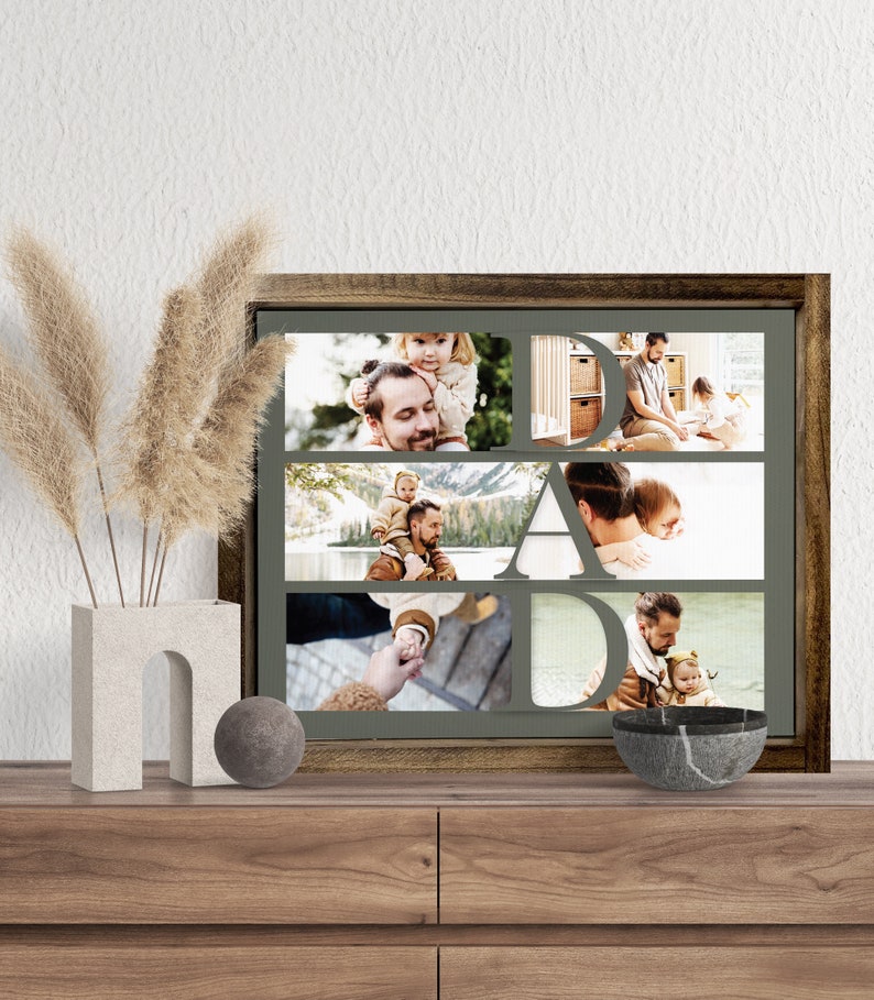 Op de afbeelding: Een ingelijste fotocollage met het woord "DAD" in grote letters. De collage bevat meerdere familiefoto's van een vader en kind. De lijst is donkerbruin en de achtergrond is een gedempt groen.
