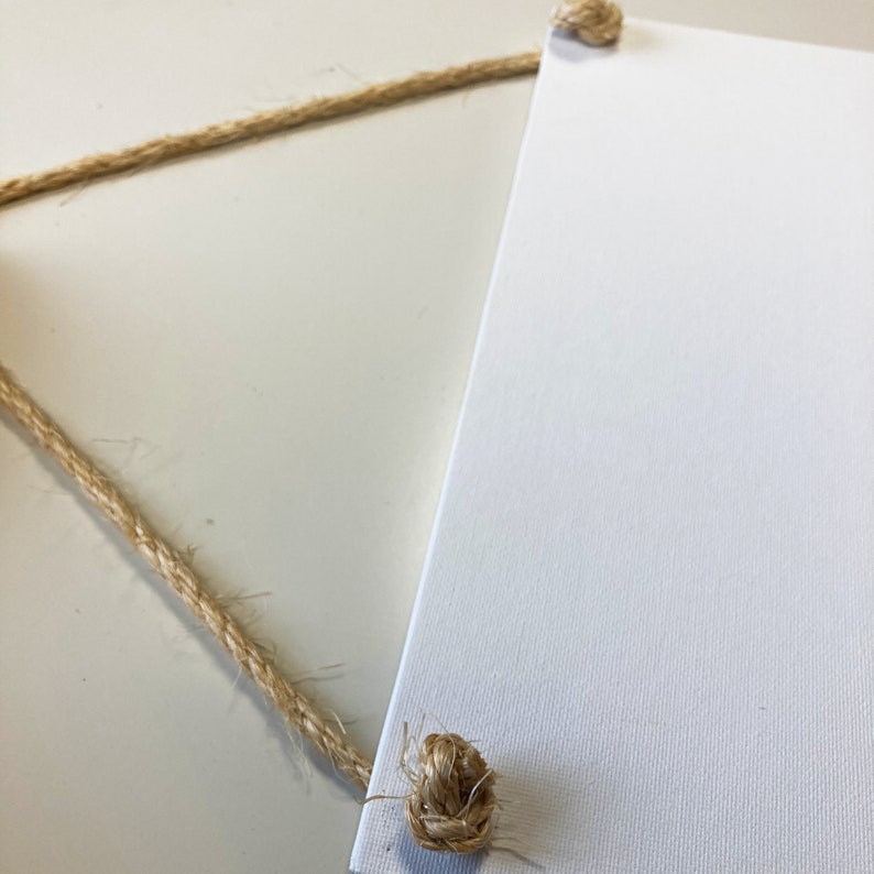 May include: A white canvas sign with two knots of natural twine attached to the top corners.