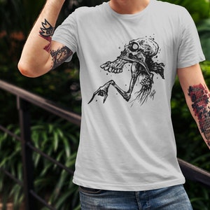 Peut inclure: T-shirt gris clair avec une illustration en noir et blanc d'une figure squelettique. Le motif graphique est centr&eacute; sur le t-shirt et repr&eacute;sente une cr&eacute;ature avec un cr&acirc;ne et des membres osseux. Le t-shirt est en mati&egrave;re souple.
