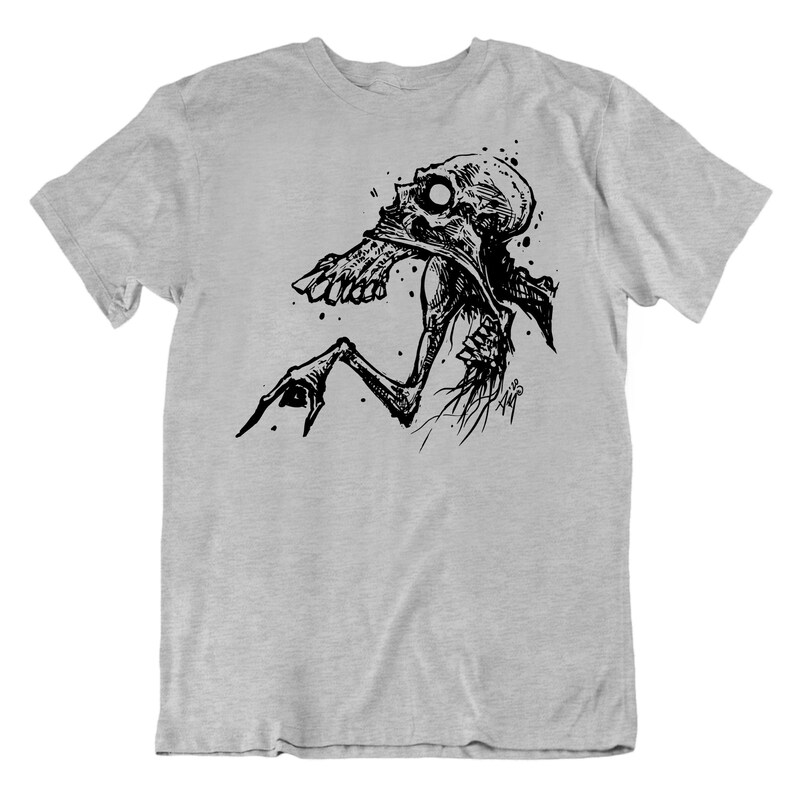Peut inclure: Un t-shirt gris clair avec une illustration en noir et blanc d'une figure squelettique. Le dessin pr&eacute;sente une t&ecirc;te en forme de cr&acirc;ne et des membres allong&eacute;s, rendus dans un style artistique d&eacute;taill&eacute; avec des &eacute;claboussures et des traits fins.