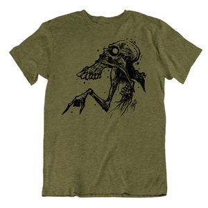 Peut inclure: T-shirt vert olive avec une illustration noire d'une cr&eacute;ature squelettique. Le dessin pr&eacute;sente une cr&eacute;ature d&eacute;taill&eacute;e de style dessin&eacute; &agrave; la main avec une bouche ouverte et une main tendue. Le t-shirt est &agrave; col rond et &agrave; manches courtes.