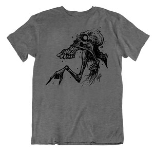 Peut inclure: T-shirt gris fonc&eacute; avec une illustration noire d'une figure squelettique. Le design pr&eacute;sente un cr&acirc;ne d&eacute;taill&eacute; et des membres allong&eacute;s. Le graphisme a un style artistique avec des &eacute;claboussures et des traits fins.