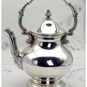 May include: A silver teapot with a curved handle and ornate detailing. The teapot has a bulbous body, a lid with a finial, and a spout with decorative elements. The handle is attached to the body with decorative flourishes. The teapot is made of a shiny, reflective metal.