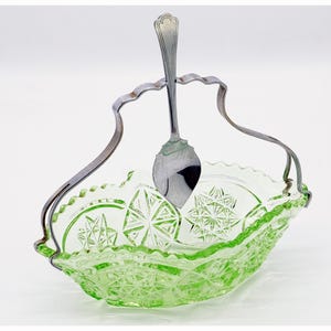 Puede incluir: Un tazón de vidrio verde con un asa y una cuchara de plata. El tazón tiene un diseño de vidrio cortado y es perfecto para servir azúcar u otras pequeñas golosinas.