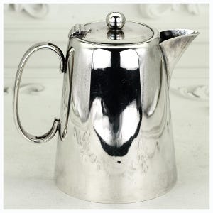 May include: A white ceramic mug with a black handle and the text "But First, Coffee" in a bold, black font. The mug is set against a blurred background, suggesting a cosy setting.