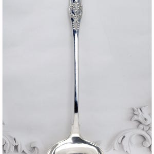 May include: A silver ladle with an ornate handle and a round bowl. The handle features detailed floral and scrollwork designs. The ladle is likely made of sterling silver and is suitable for serving soups and sauces.
