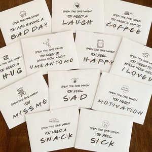 May include: Ten white cards with black text and illustrations. Each card has a different message, such as "Open the one when you need a hug" or "Open the one when you need a laugh".