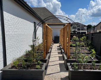 Könnte beinhalten: Ein Garten im Hinterhof mit Hochbeeten und einem Holz-Gitterbogen. Die Beete sind mit Pflanzen und Blumen gefüllt. Der Garten ist von einer weißen Backsteinmauer und einem schwarzen Zaun umgeben.