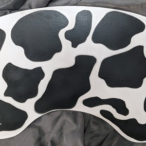 May include: A white and black cow print design on a curved, flexible surface. The surface is made of a thick, durable material.