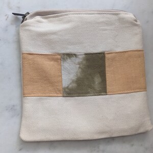 May include: A white canvas zippered pouch with a brown and green tie-dye design. The pouch has a zipper closure and a rectangular shape.