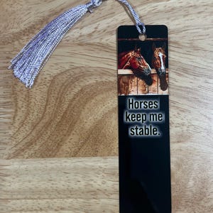 May include: Black bookmark with a silver tassel. The bookmark features a picture of two horses looking out of a stable with the text "Horses keep me stable."