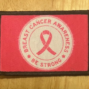 May include: Pink fabric patch with a white circle containing a pink ribbon and the text "Breast Cancer Awareness Be Strong".