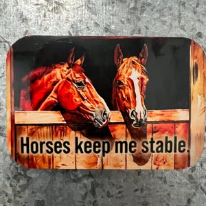 May include: Rectangular magnet featuring two brown horses in a stable. The horses are looking out from the wooden stall. The text "Horses keep me stable" is printed in white on the bottom of the magnet.