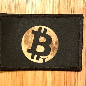 May include: Black rectangular patch featuring a gold Bitcoin symbol set against a full moon design. A small silhouette of a person with arms raised is below the moon. The patch has a black border.