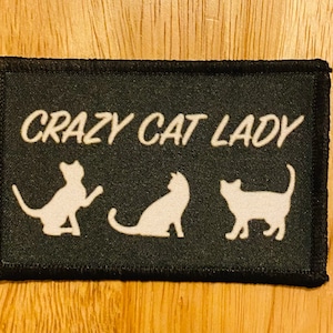 May include: Black patch with white text that reads "Crazy Cat Lady" and three white silhouettes of cats.