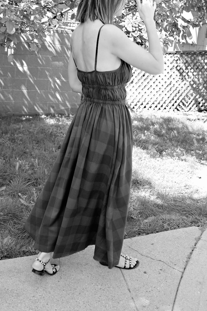 May include: A woman wearing a black and white plaid maxi dress with a gathered waist and thin straps. She is wearing black sandals with silver studs.