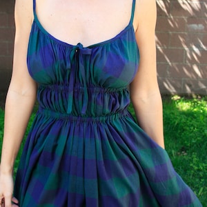 May include: A woman wearing a blue and green plaid sundress with a gathered waist and thin straps.