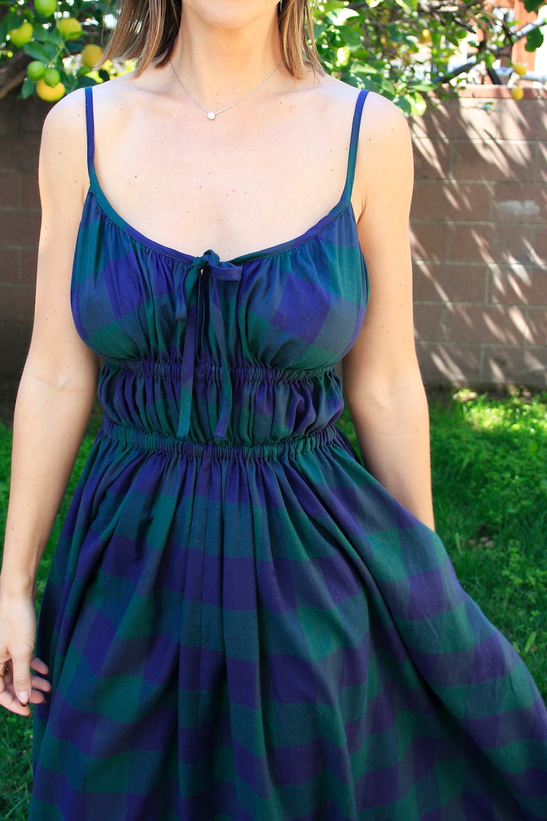May include: A woman wearing a blue and green plaid sundress with a gathered waist and thin straps.