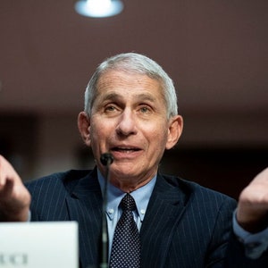 May include: A man with gray hair and a blue suit speaks at a podium with the text "Dr. Fauci" on it. He is gesturing with both hands.