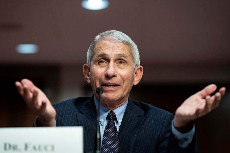 May include: A man with gray hair and a blue suit speaks at a podium with the text "Dr. Fauci" on it. He is gesturing with both hands.