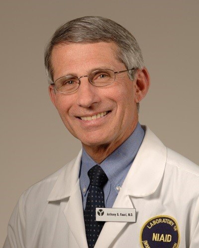 May include: A man wearing a white lab coat with a blue shirt and a dark tie. He is smiling and has a name tag that reads "Anthony S. Fauci, M.D." and a badge that reads "Laboratory of NIAID".