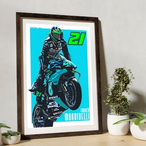 May include: A digital illustration of a motorcycle racer wearing a green helmet and a blue and green racing suit. The racer is on a blue and green motorcycle with the number 21 on the side. The background is a light blue colour. The text "Franco Morbidelli" is at the bottom of the image.