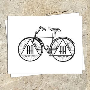 May include: Black and white illustration of a bicycle with the words "AA" and the words "Unity, Service, Recovery" on each wheel.