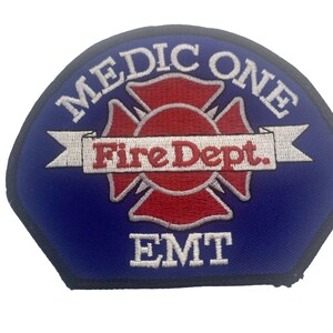 Op de afbeelding: Een blauw en rood geborduurd embleem met de woorden "MEDIC ONE" bovenaan. In het midden staat een rood Maltezer kruis met "Fire Dept." op een witte banner. Het woord "EMT" staat onderaan.