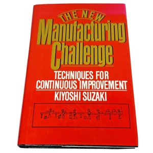May include: A red hardcover book titled "The New Manufacturing Challenge: Techniques for Continuous Improvement" by Kiyoshi Suzaki. The book cover features a gold title and a black and white illustration of stick figures working on an assembly line.