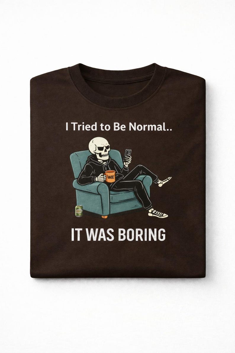 May include: Brown t-shirt featuring a skeleton in a hoodie, seated in a teal armchair, holding a phone. The skeleton has a coffee mug that says "ME". The text on the shirt reads "I Tried to Be Normal.. IT WAS BORING".