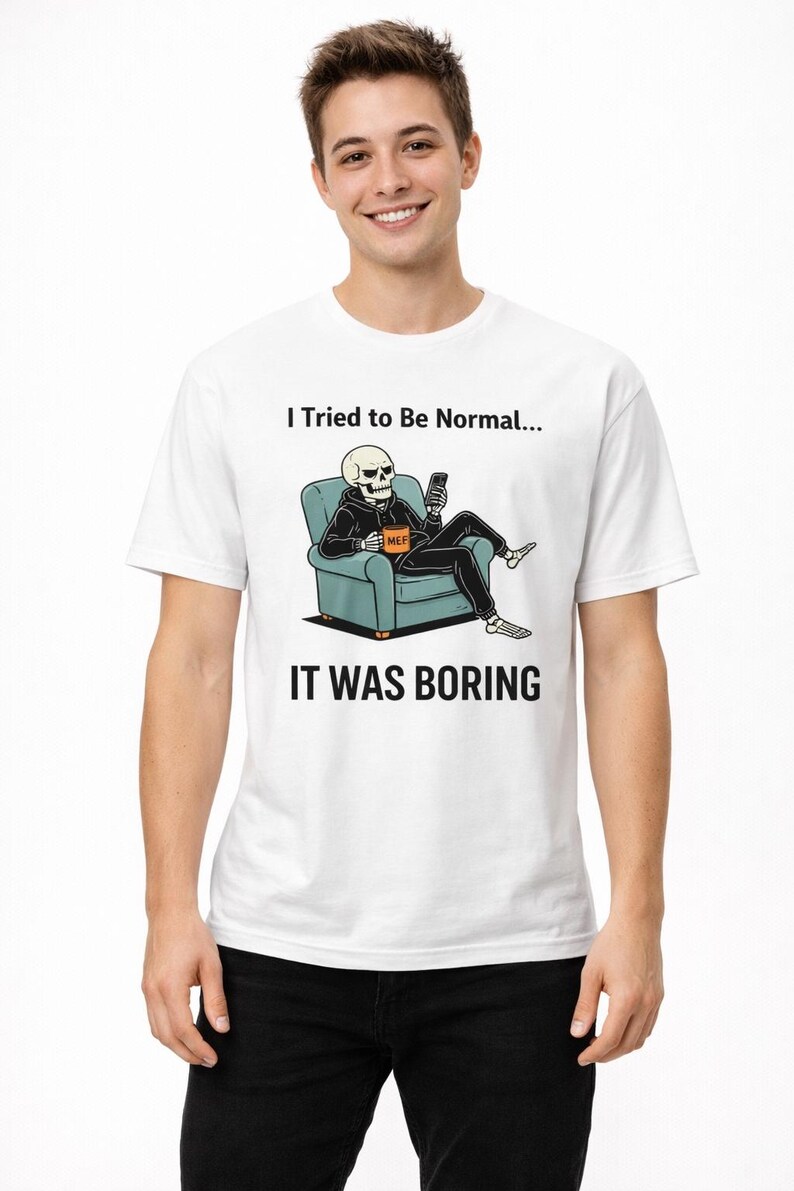 May include: White t-shirt with a graphic of a skeleton in a hoodie, seated on a blue armchair, holding a phone. The text "I Tried to Be Normal... IT WAS BORING" is printed above and below the graphic.