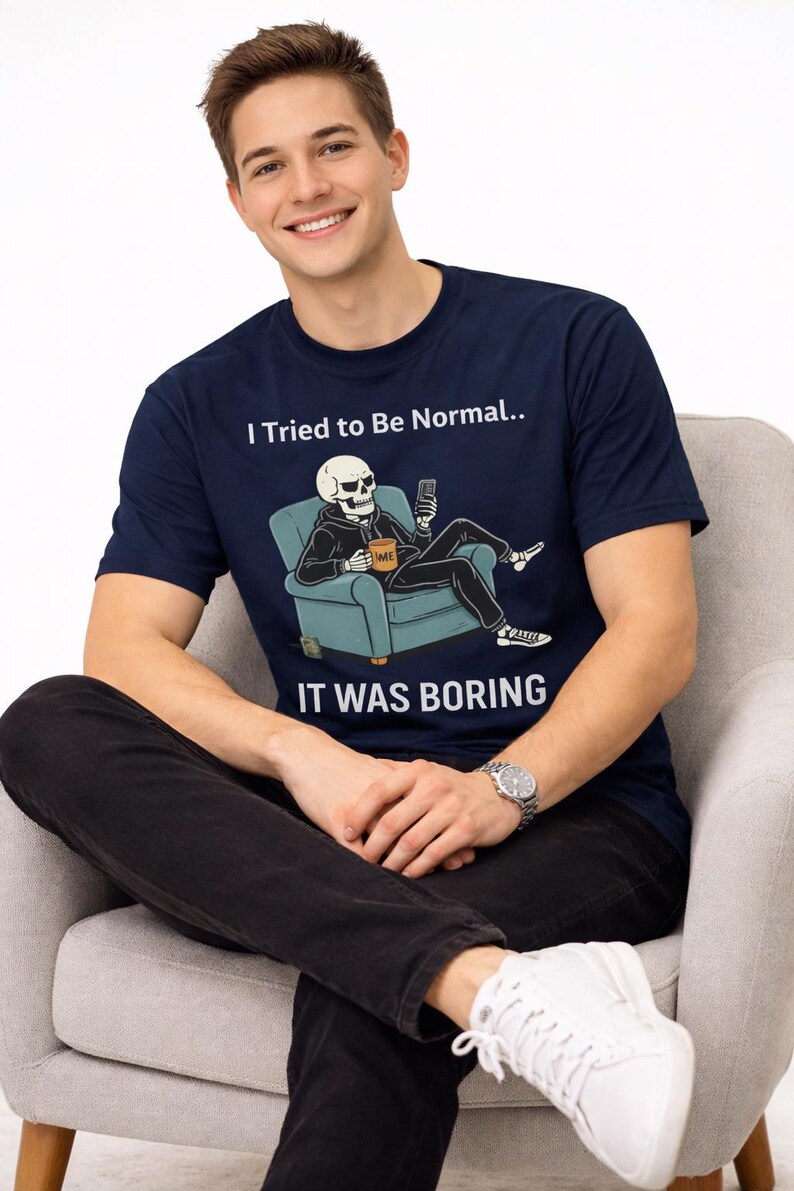 May include: Navy blue t-shirt with the text "I Tried to Be Normal.. IT WAS BORING" and a graphic of a skeleton relaxing on a chair. The skeleton is holding a phone and a mug. The person is wearing black pants and white sneakers.