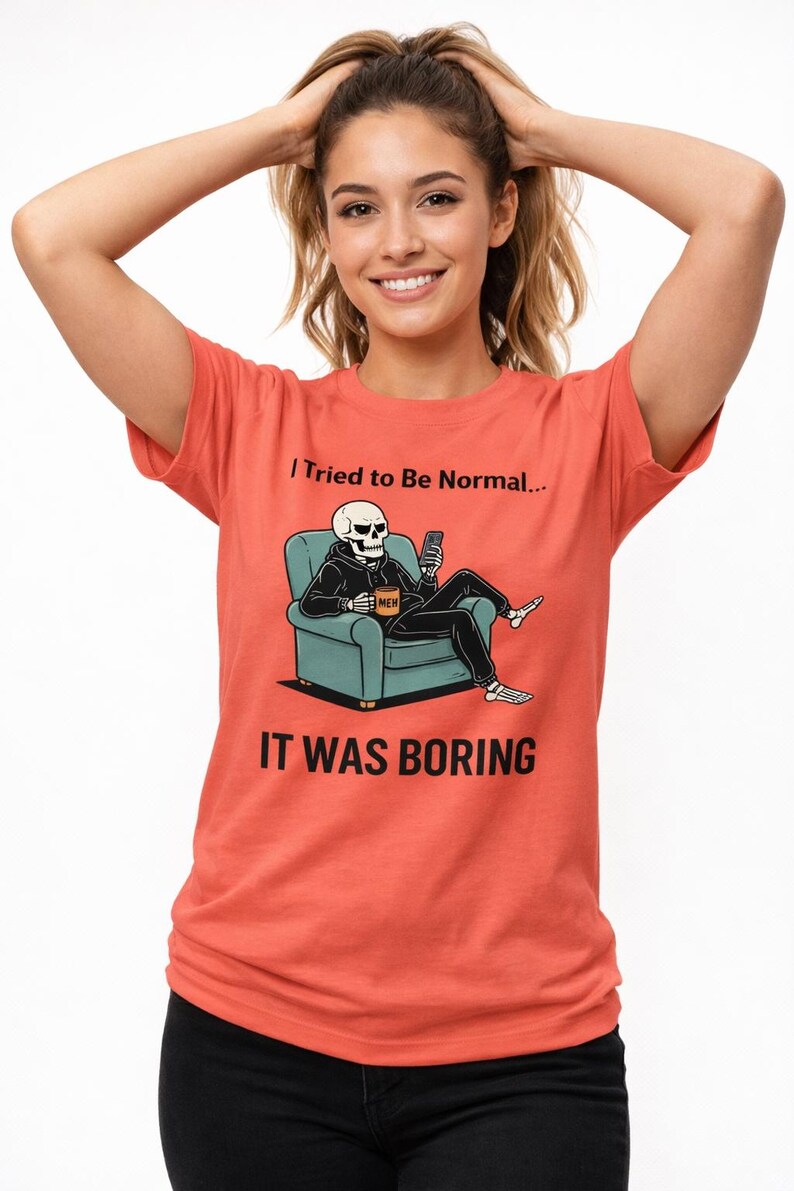 May include: Coral-colored t-shirt with the text "I Tried to Be Normal... IT WAS BORING." The shirt features a graphic of a skeleton in a hoodie, seated in a teal armchair, holding a phone and a coffee mug.