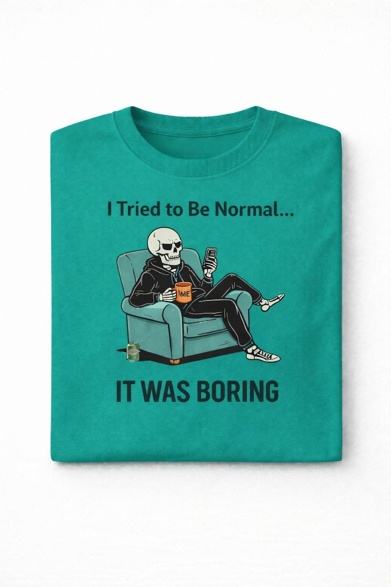 May include: Teal crew neck t-shirt with the text "I Tried to Be Normal... It Was Boring." The graphic shows a skeleton in a hoodie sitting in a chair, using a phone. The skeleton is holding a mug that says "TIME".