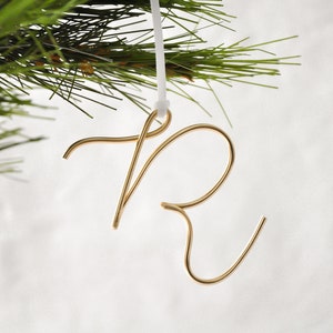 May include: Gold wire ornament shaped like the letter "R" hanging from a white string.