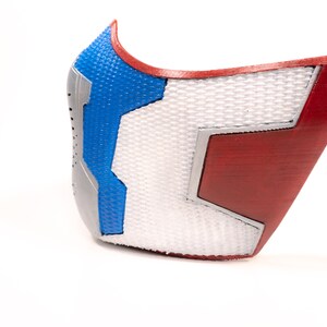 Pode incluir: Uma m&aacute;scara impressa em 3D com um design vermelho, branco e azul. A m&aacute;scara tem uma superf&iacute;cie texturizada e uma forma geom&eacute;trica.
