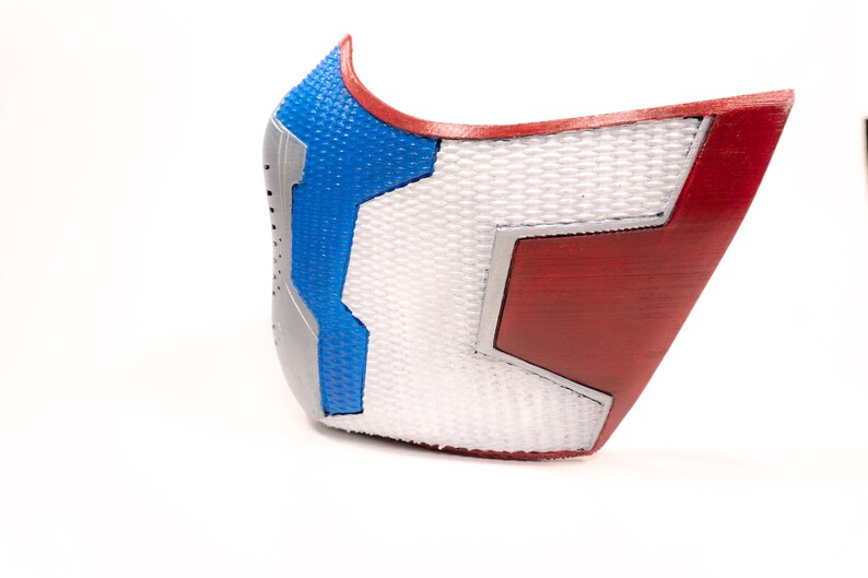 Pode incluir: Uma m&aacute;scara impressa em 3D com um design vermelho, branco e azul. A m&aacute;scara tem uma superf&iacute;cie texturizada e uma forma geom&eacute;trica.