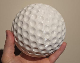 May include: A spherical white object with a textured surface featuring numerous small, uniform circular indentations across its entire exterior. The object has a smooth, glossy finish and is shaped like a standard golf ball, displaying a repeating pattern of dimples.