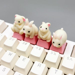 Może przedstawiać: Cztery białe klawisze w kształcie królika z różowymi akcentami umieszczone na białej klawiaturze. Klawisze są oznaczone liczbami 2, 3, 4 i 5.