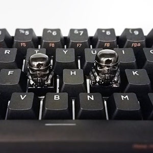 May include: Two black and silver Star Wars Stormtrooper keycaps on a black keyboard. The keycaps are on the H and U keys.