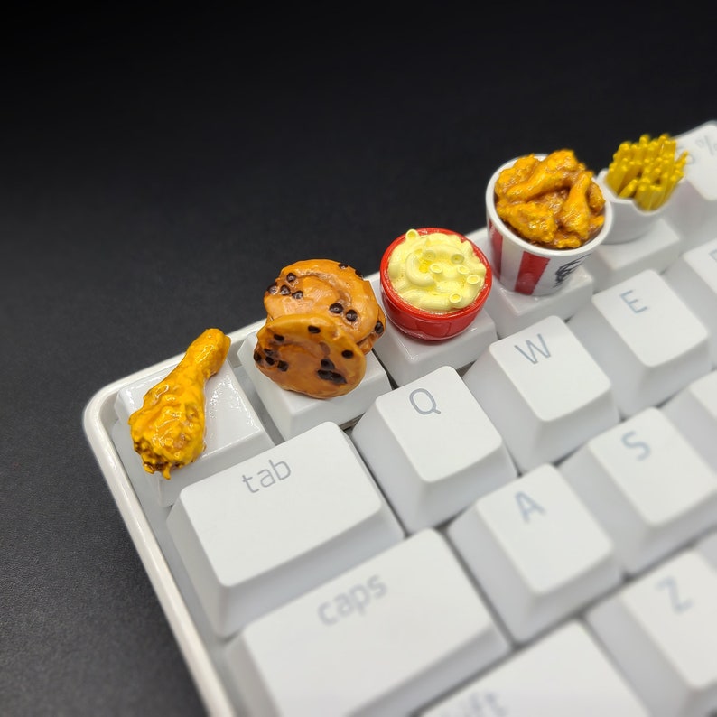May include: A white keyboard with miniature food items on the keys. The food items include a fried chicken leg, a cinnamon roll, a bowl of macaroni and cheese, a bucket of fried chicken wings, and a small container of french fries.