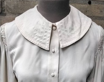 May include: A white long-sleeved blouse with a large, rounded collar and a button-up front.