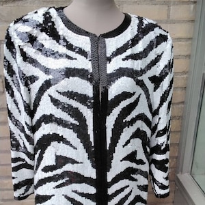 May include: A black and white zebra print jacket with a long sleeve and a front zip closure. The jacket is made of sequins.