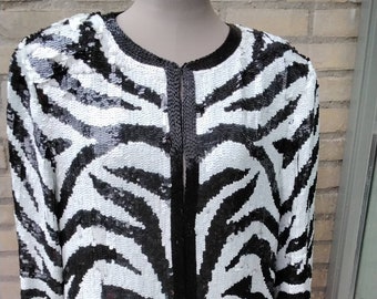 May include: A black and white zebra print jacket with a long sleeve and a front zipper closure. The jacket is made of sequins.