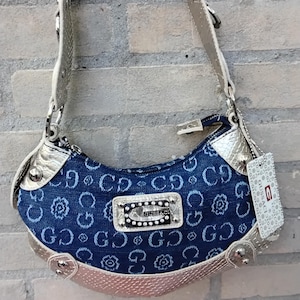 May include: A small denim handbag with a silver strap and trim. The bag has a repeating pattern of the letters "G" and "C" in a floral design. A rectangular label with the name "GUSSACI" is on the front.