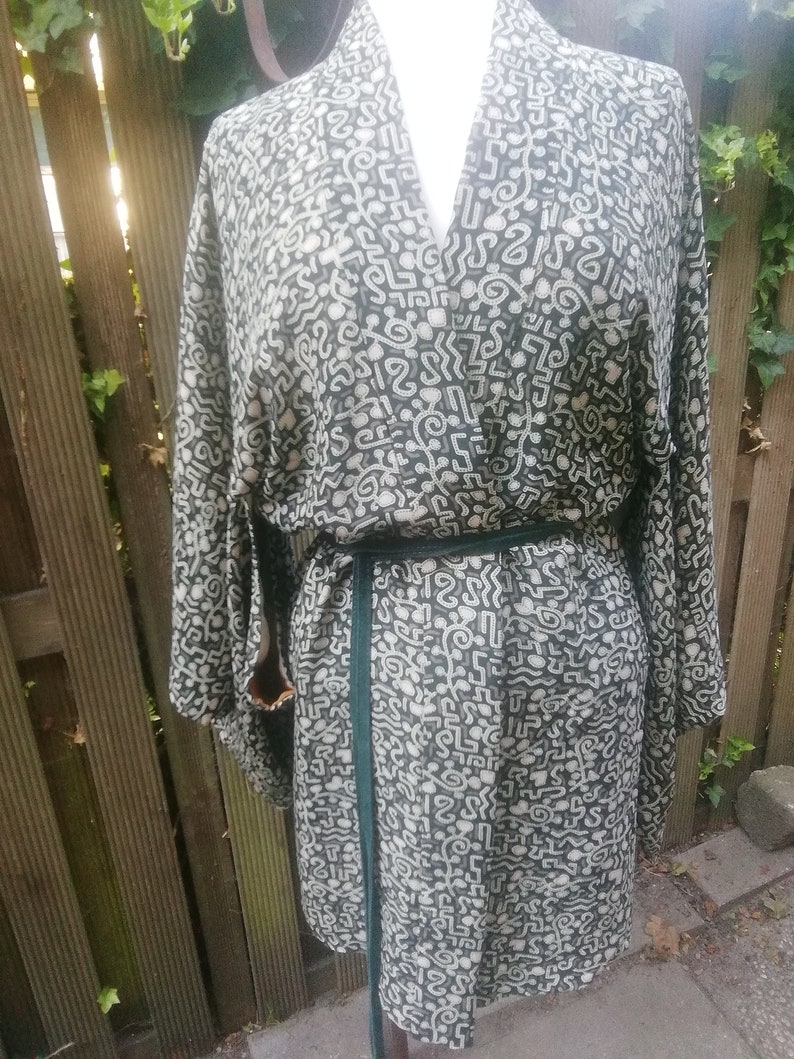 May include: A black and white patterned kimono with a green sash. The pattern is made up of abstract shapes and lines.