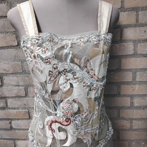 May include: A white and beige mesh top with a floral design and beaded embellishments. The top has a square neckline and thin straps.