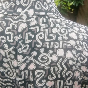 May include: Black fabric with a white and pink abstract pattern. The pattern features a variety of shapes and lines, including circles, squares, and squiggles.